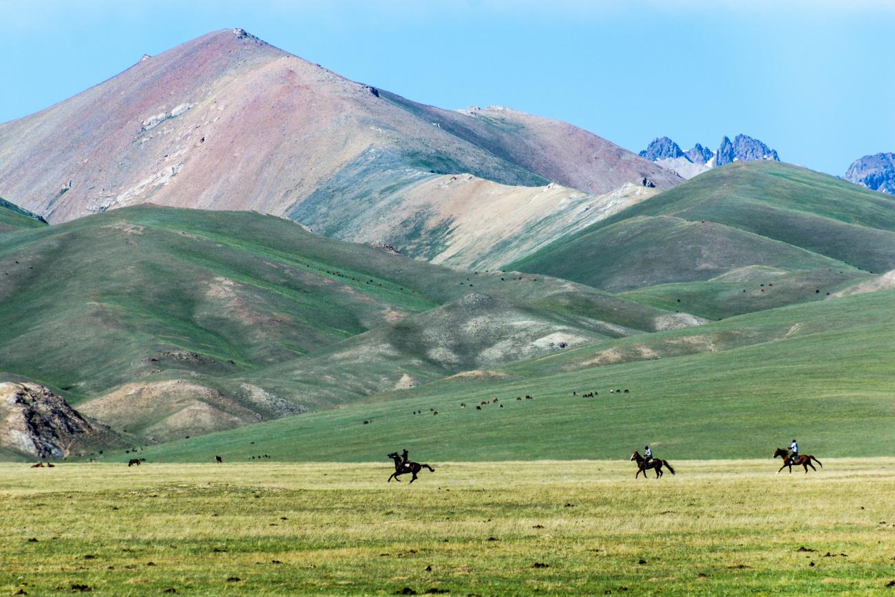 Three people horse riding in a valley of Kyrgyz mountains