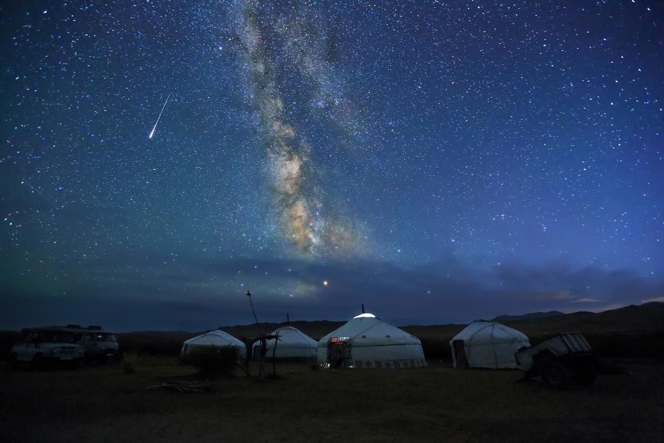 Traditional ger camps in Mongolia during the night with the milky way and a shooting star above them