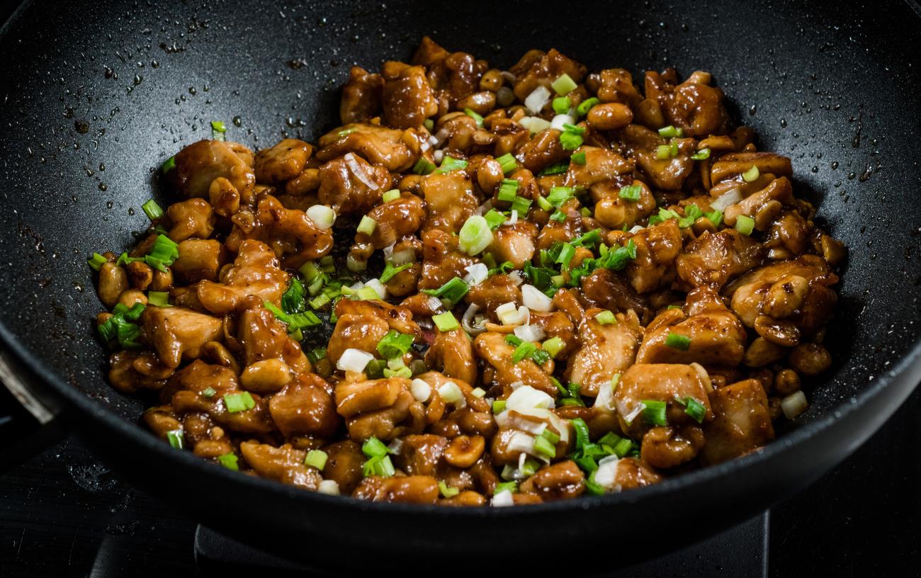 Closeup of kung pao chicken being cooked in a wok