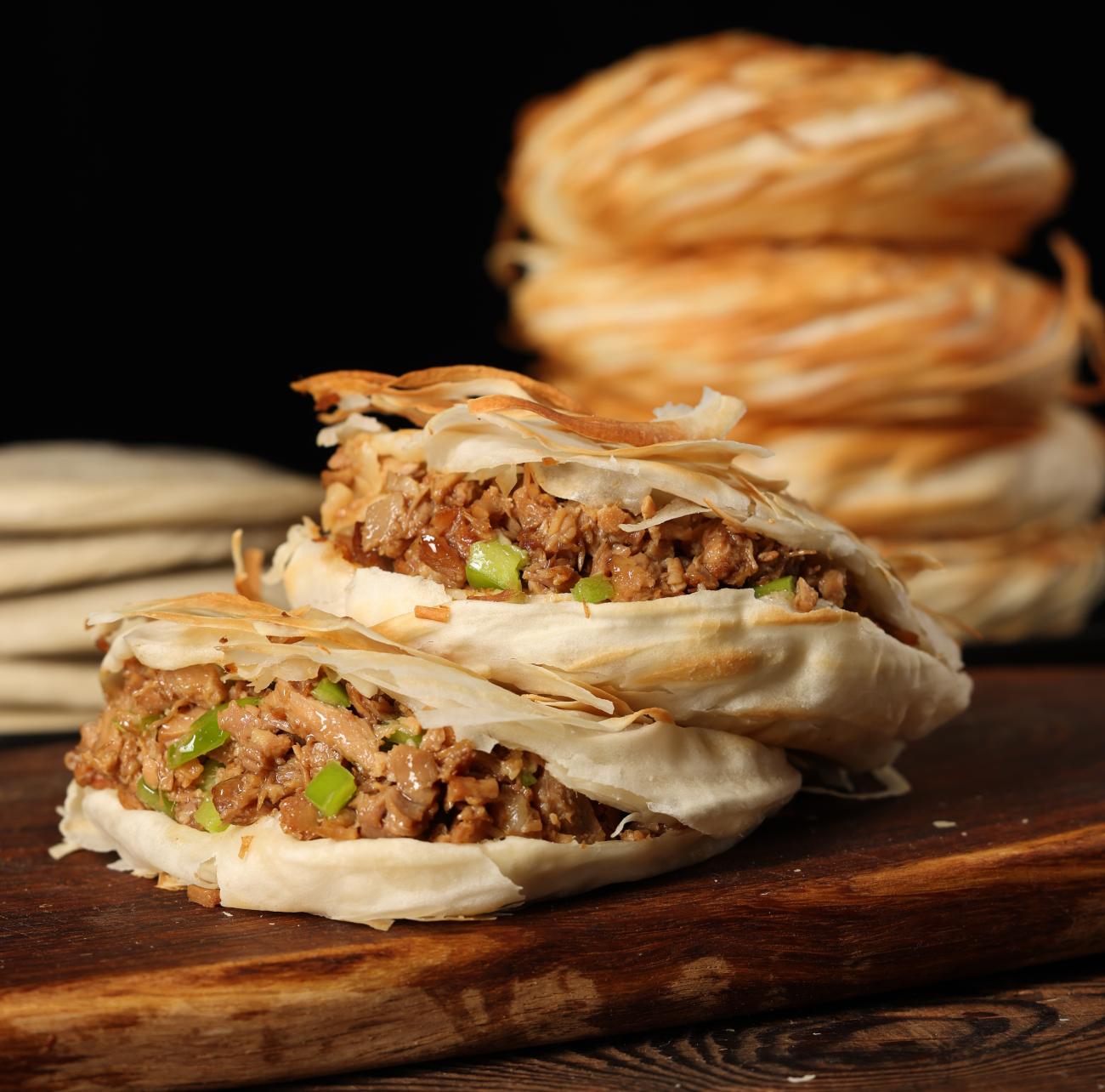 Closeup of two Chinese burgers called Roujiamo with a stack of 3 buns in the back